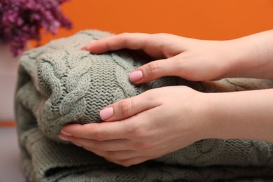Photo of Woman with folded woolen blanket near orange wall indoors, closeup
