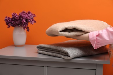 Photo of Woman with folded woolen blankets near orange wall indoors, closeup