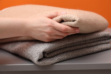 Photo of Woman with folded woolen blankets near orange wall indoors, closeup