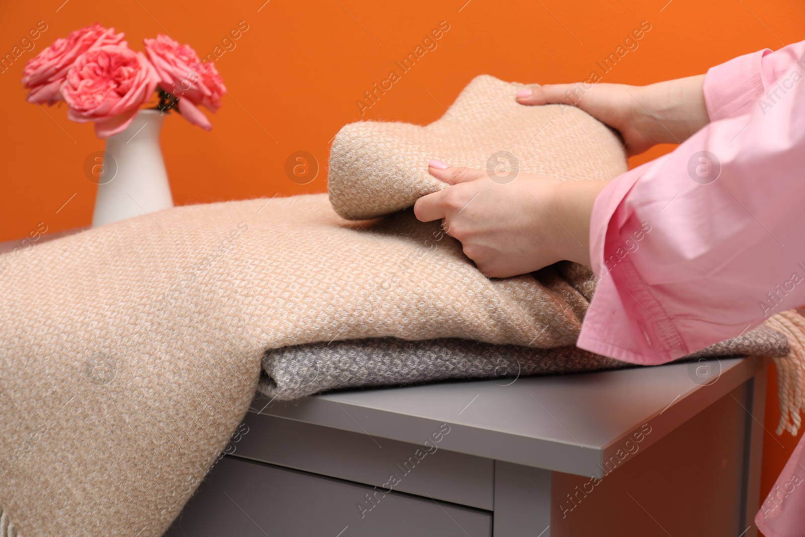 Woman folding woolen blanket near orange wall indoors, closeup Photo of Woman folding woolen blanket near orange wall indoors, closeup