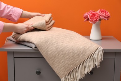 Photo of Woman folding woolen blanket near orange wall indoors, closeup