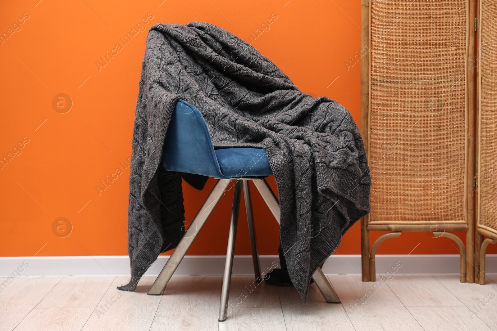 Comfortable armchair with woolen blanket near orange wall indoors Photo of Comfortable armchair with woolen blanket near orange wall indoors