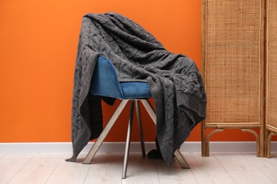 Photo of Comfortable armchair with woolen blanket near orange wall indoors