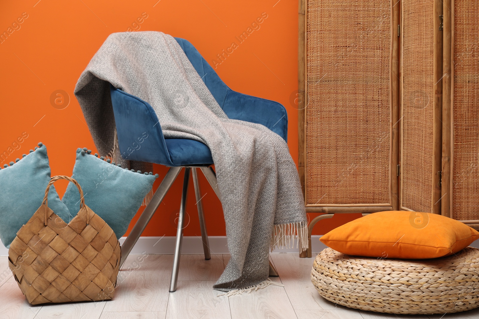 Comfortable armchair with woolen blanket and pillows near orange wall indoors Photo of Comfortable armchair with woolen blanket and pillows near orange wall indoors