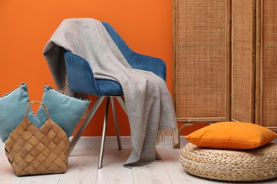 Photo of Comfortable armchair with woolen blanket and pillows near orange wall indoors