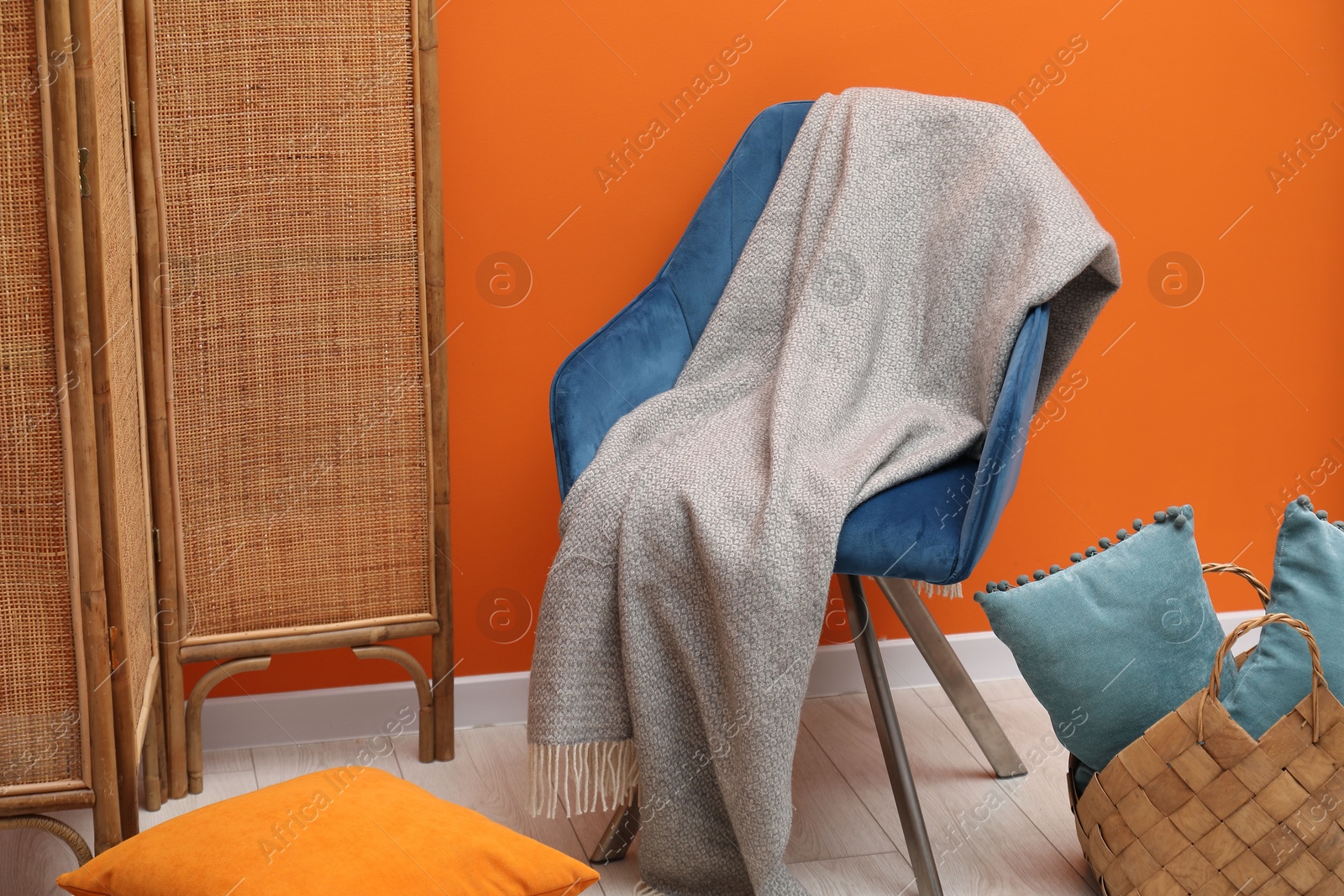 Comfortable armchair with woolen blanket and pillows near orange wall indoors Photo of Comfortable armchair with woolen blanket and pillows near orange wall indoors