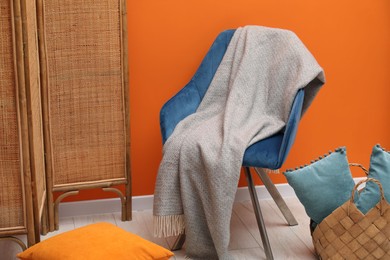 Photo of Comfortable armchair with woolen blanket and pillows near orange wall indoors
