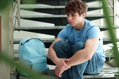 Photo of Teen problems. Upset teenage boy on stairs indoors