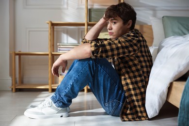 Photo of Teen problems. Depressed teenage boy near bed at home