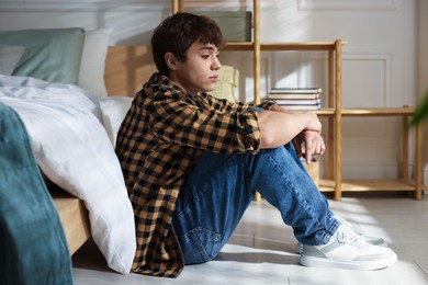 Photo of Teen problems. Depressed teenage boy near bed at home