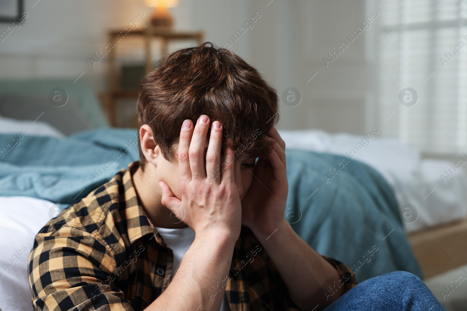 Teen problems. Depressed teenage boy near bed at home Photo of Teen problems. Depressed teenage boy near bed at home