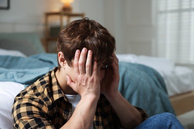 Photo of Teen problems. Depressed teenage boy near bed at home