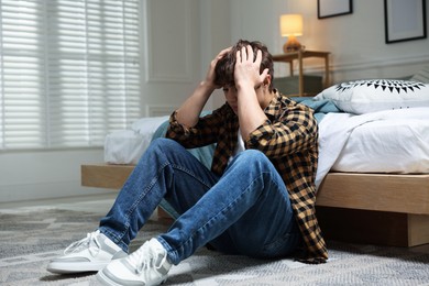 Photo of Teen problems. Depressed teenage boy on floor at home