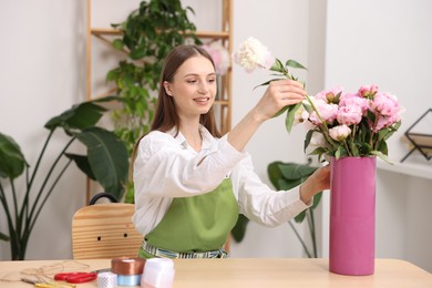 Photo of Florist making bouquet of peonies at table in flower shop