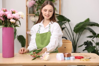 Photo of Florist making bouquet of peonies at table in flower shop
