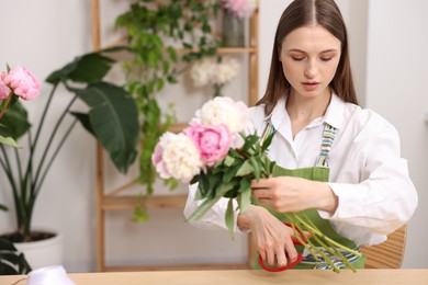 Photo of Florist making bouquet of peonies at table in flower shop, space for text