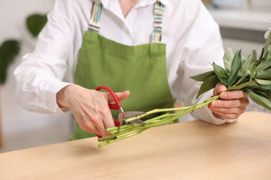 Photo of Florist making bouquet of flowers at wooden table in flower shop, closeup