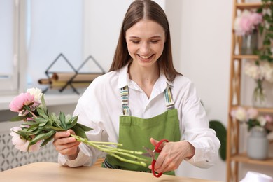Photo of Florist making bouquet of peonies at table in flower shop