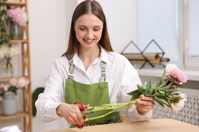 Photo of Florist making bouquet of peonies at table in flower shop