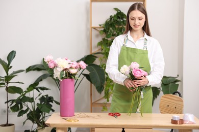 Photo of Florist making bouquet of peonies at wooden table in flower shop