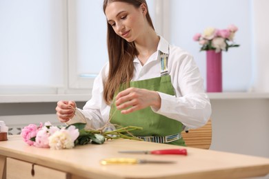 Photo of Florist making bouquet of peonies at wooden table in flower shop