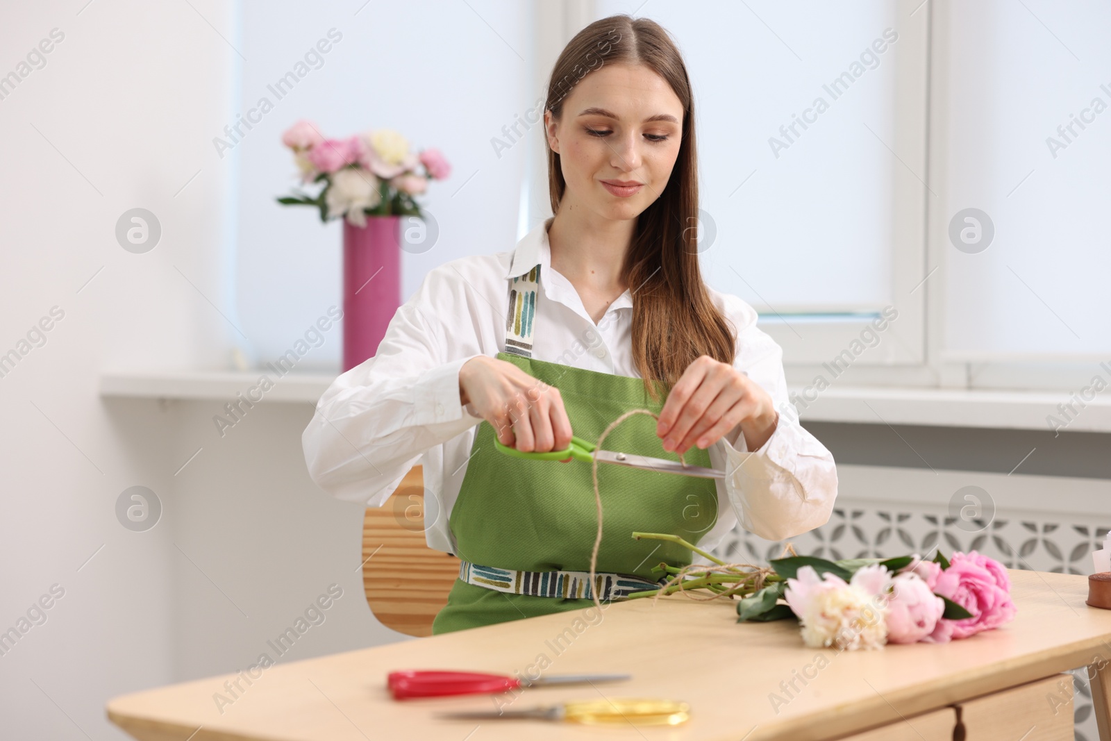 Florist making bouquet of peonies at wooden table in flower shop Photo of Florist making bouquet of peonies at wooden table in flower shop