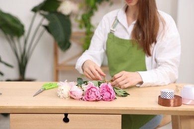 Photo of Florist making bouquet of peonies at wooden table in flower shop, closeup. Space for text