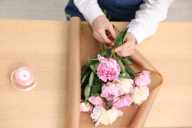 Photo of Florist making bouquet of peonies at wooden table, above view