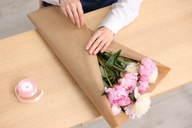 Photo of Florist making bouquet of peonies at wooden table, above view