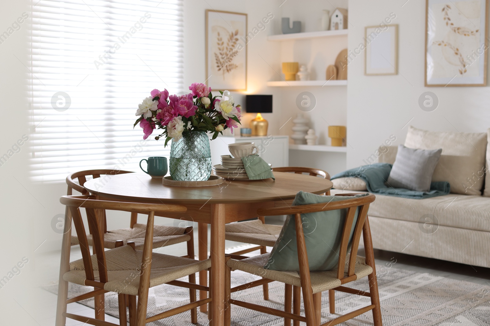 Dining table with beautiful flowers and dishware in room. Interior design Photo of Dining table with beautiful flowers and dishware in room. Interior design