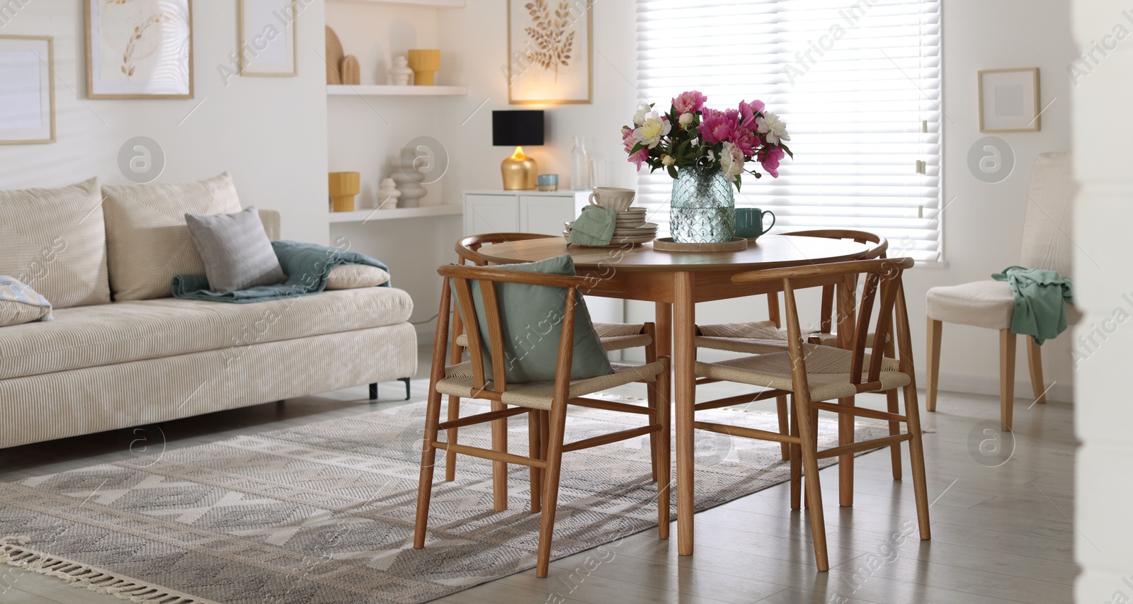Dining table with beautiful flowers and dishware in room. Interior design Photo of Dining table with beautiful flowers and dishware in room. Interior design