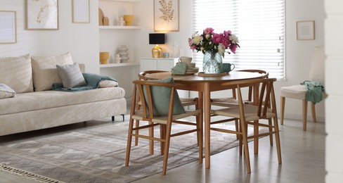 Photo of Dining table with beautiful flowers and dishware in room. Interior design