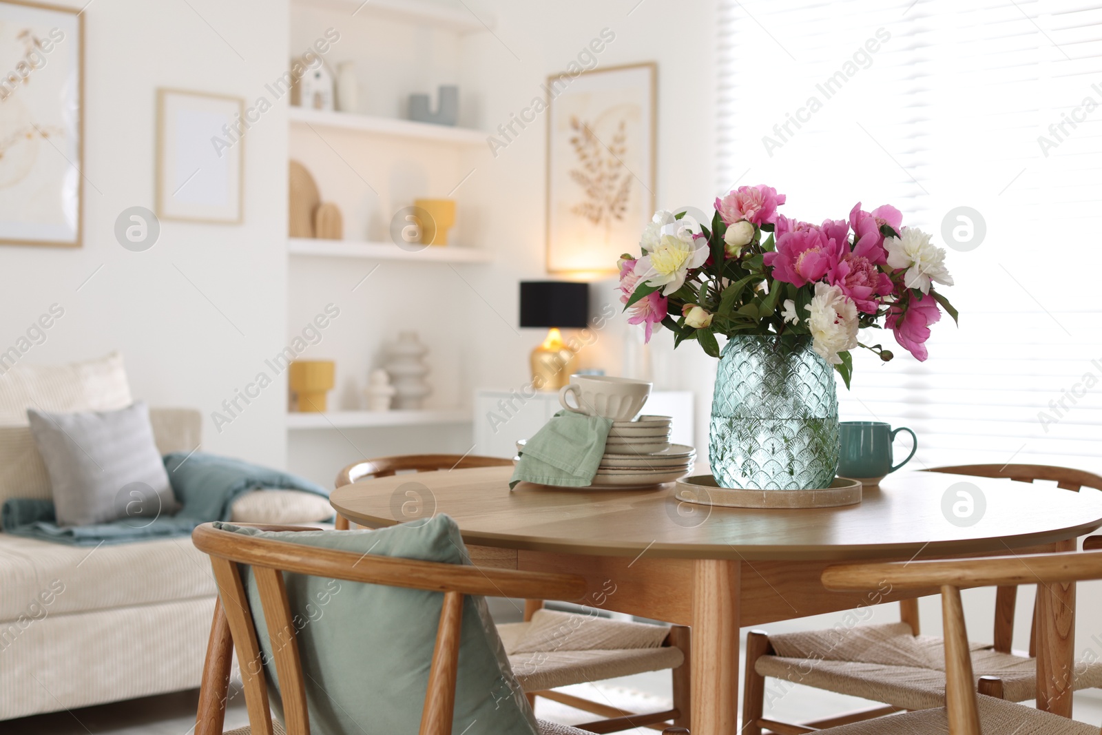 Dining table with beautiful flowers and dishware in room, space for text. Interior design Photo of Dining table with beautiful flowers and dishware in room, space for text. Interior design