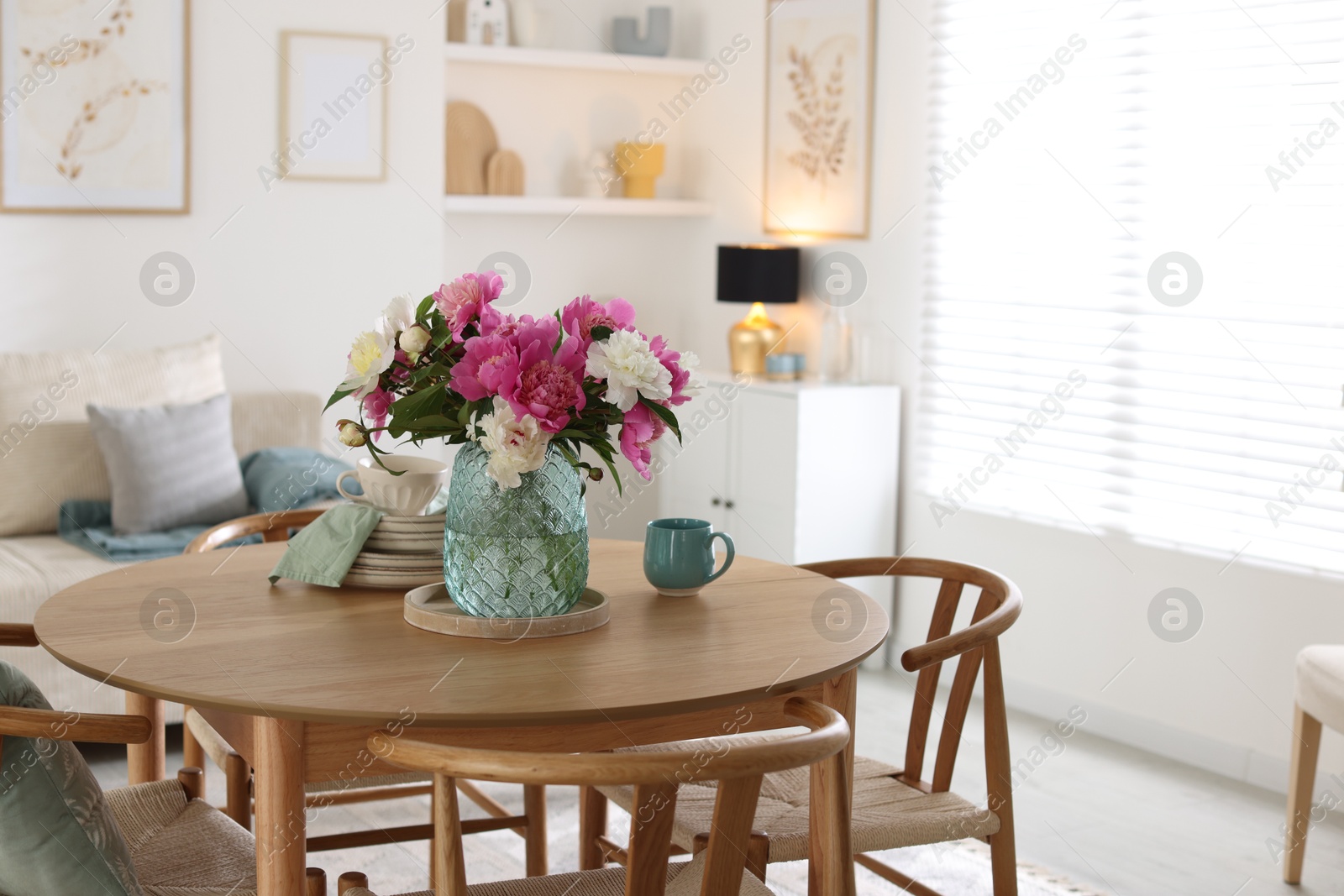 Dining table with beautiful flowers and dishware in room. Interior design Photo of Dining table with beautiful flowers and dishware in room. Interior design