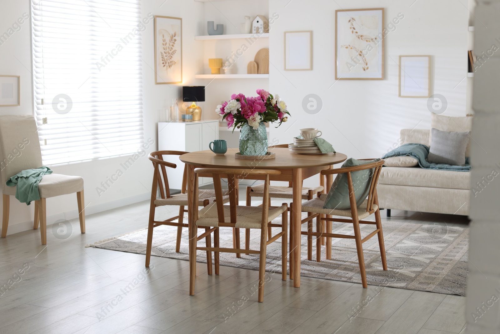 Dining table with beautiful flowers and dishware in room. Interior design Photo of Dining table with beautiful flowers and dishware in room. Interior design