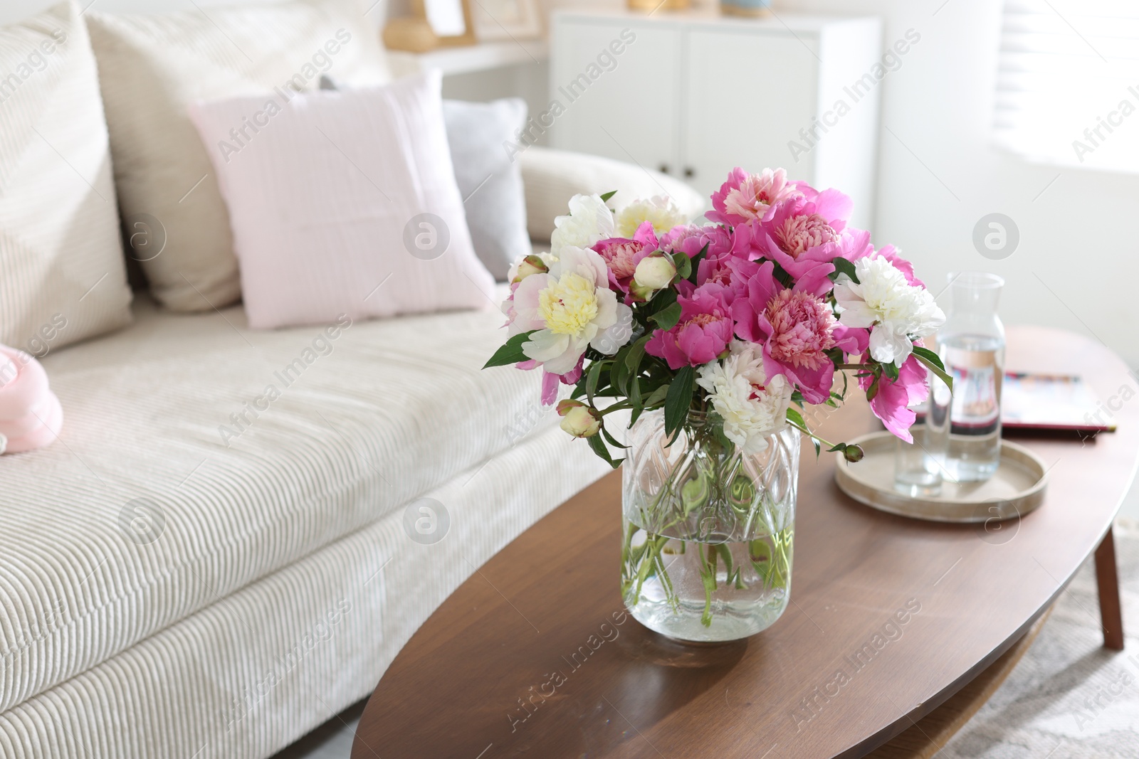Bouquet of beautiful peonies and water on coffee table indoors, space for text. Interior design Photo of Bouquet of beautiful peonies and water on coffee table indoors, space for text. Interior design