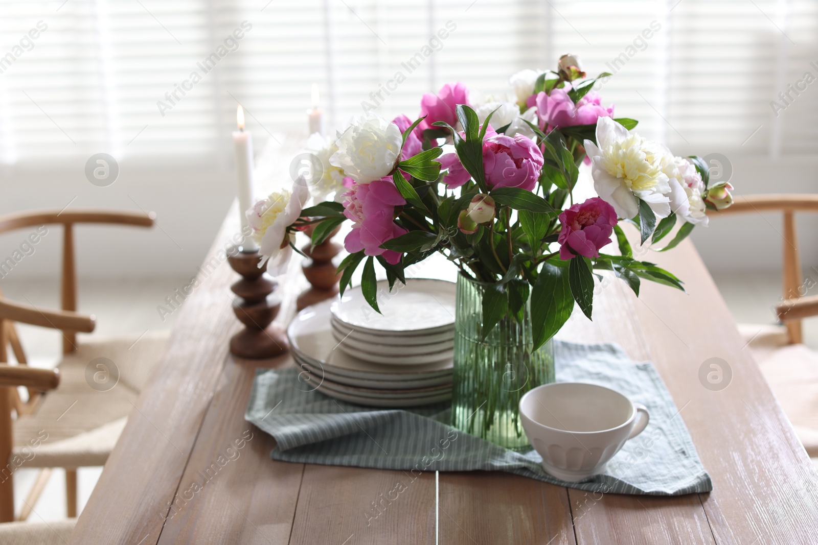 Dining table with beautiful flowers and dishware in room. Interior design Photo of Dining table with beautiful flowers and dishware in room. Interior design