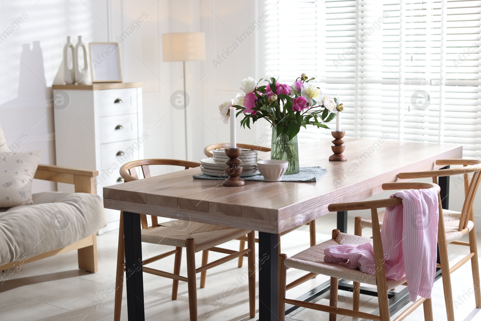Dining table with beautiful flowers and dishware in room. Interior design Photo of Dining table with beautiful flowers and dishware in room. Interior design