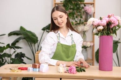 Photo of Florist making bouquet of peonies at table in flower shop