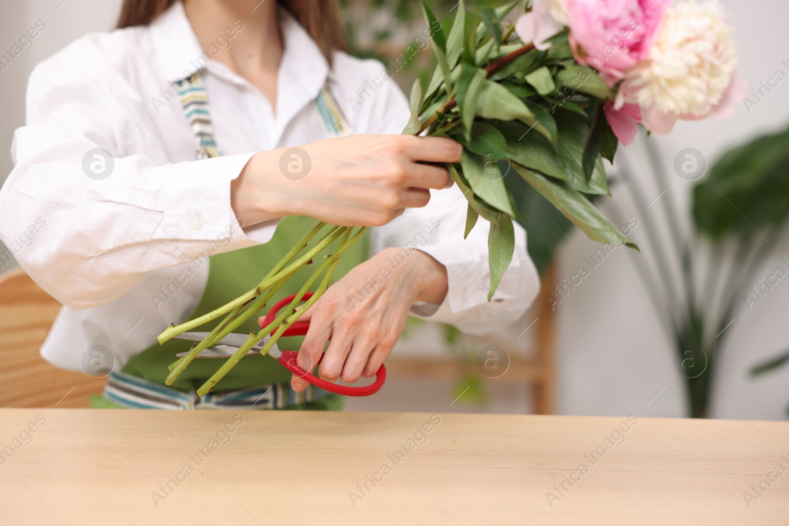 Florist making bouquet of peonies at wooden table in flower shop, closeup Photo of Florist making bouquet of peonies at wooden table in flower shop, closeup