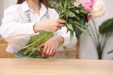 Photo of Florist making bouquet of peonies at wooden table in flower shop, closeup