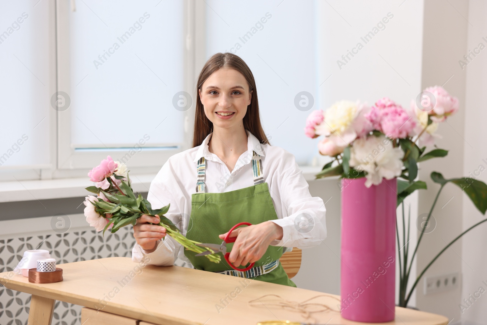 Photo of Florist making bouquet of peonies at wooden table in flower shop