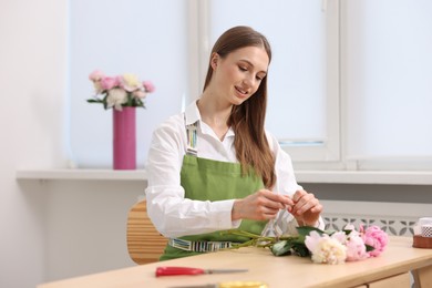 Photo of Florist making bouquet of peonies at wooden table in flower shop