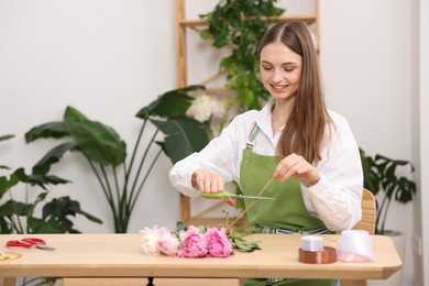 Photo of Florist making bouquet of peonies at wooden table in flower shop, space for text