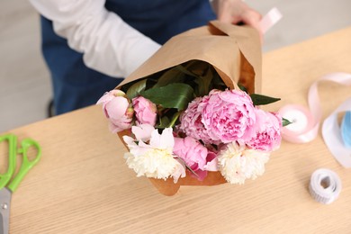 Photo of Florist with beautiful bouquet of peonies at wooden table, above view