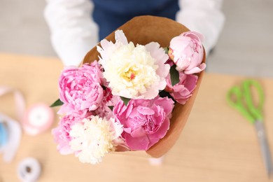 Photo of Florist with beautiful bouquet of peonies at table, top view