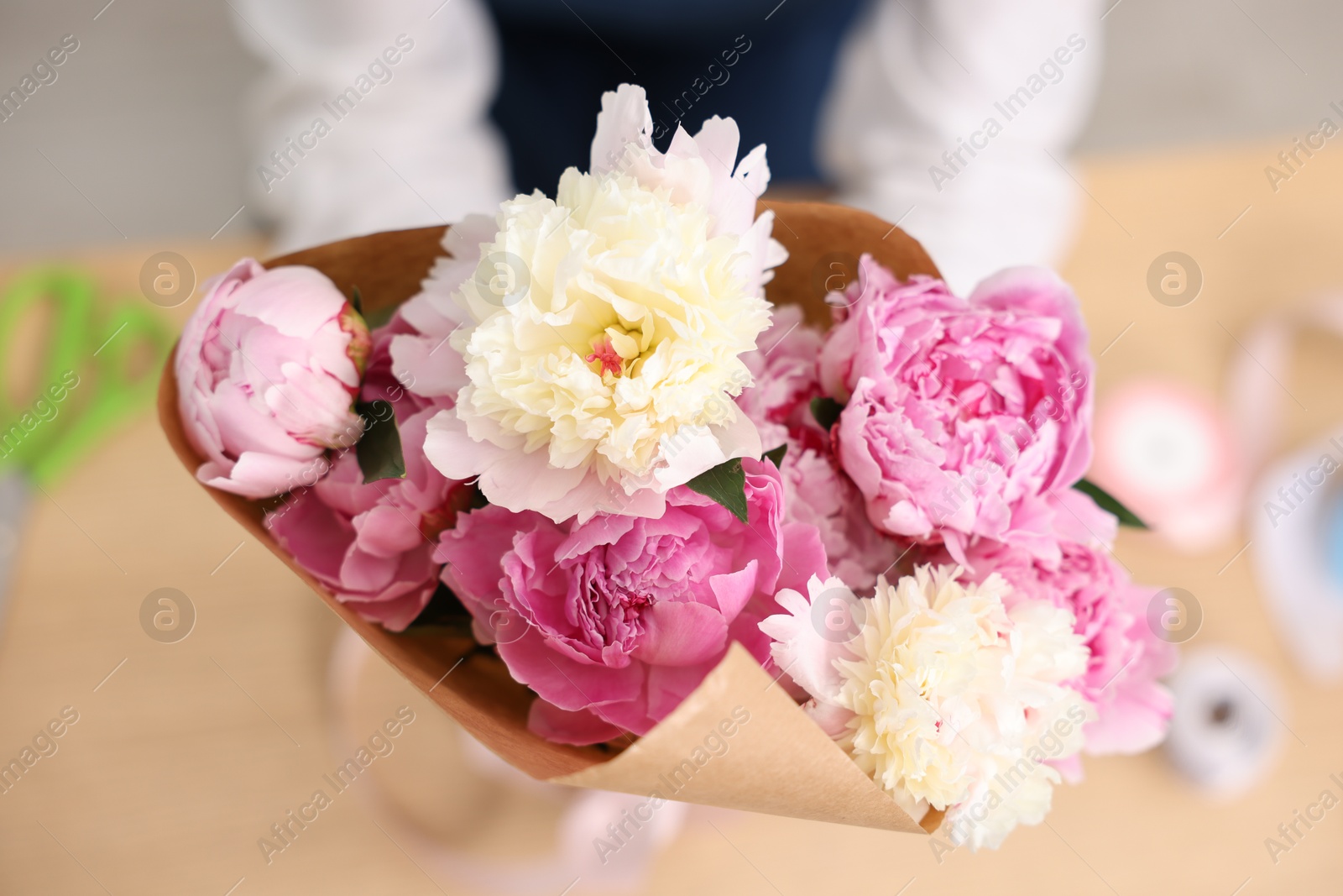 Florist with beautiful bouquet of peonies at table, top view Photo of Florist with beautiful bouquet of peonies at table, top view