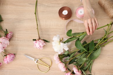 Photo of Florist making bouquet of flowers at wooden table, top view