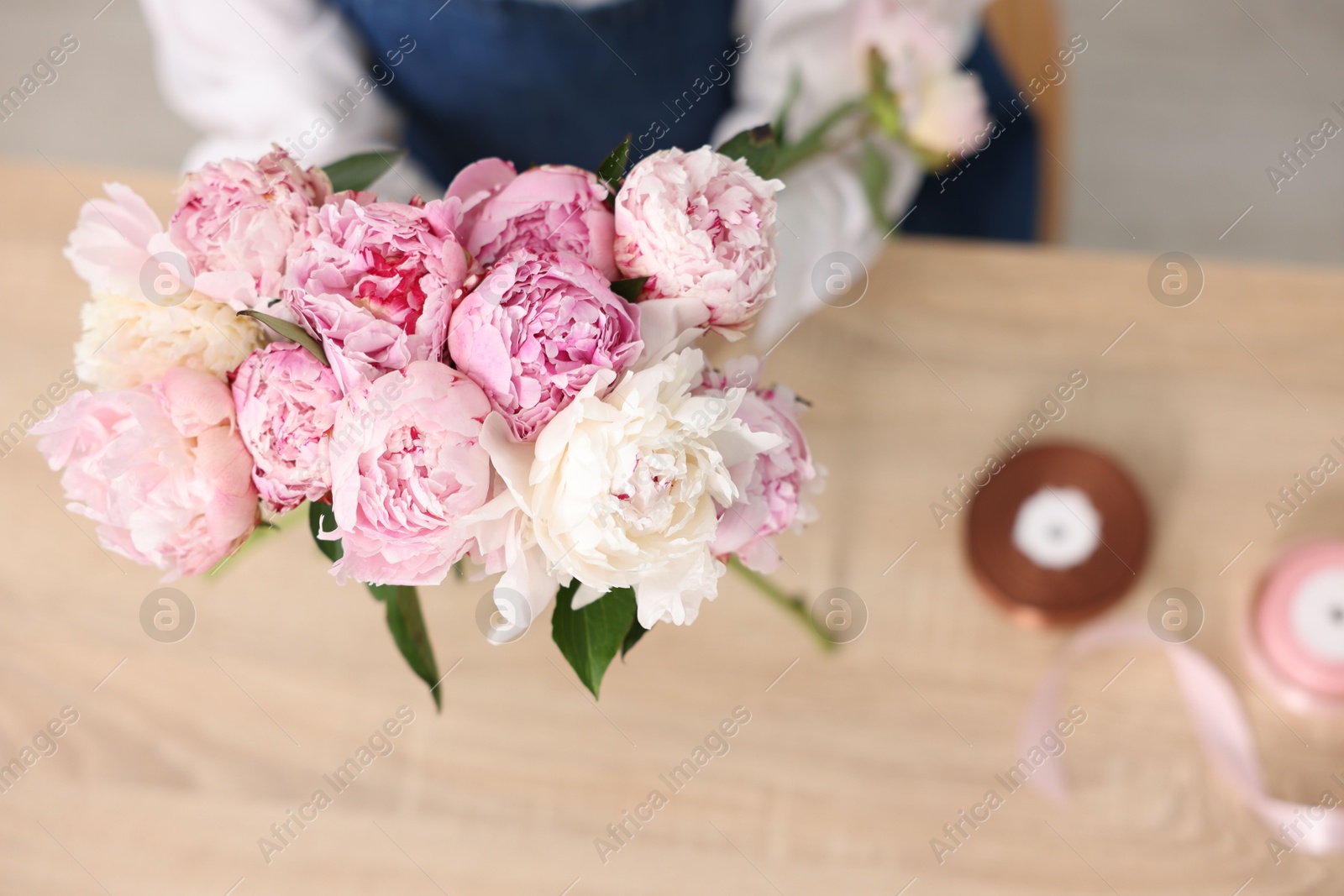 Florist with beautiful bouquet of peonies at table, above view Photo of Florist with beautiful bouquet of peonies at table, above view