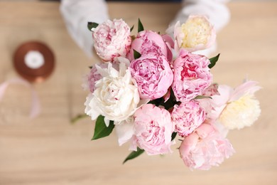 Photo of Florist with beautiful bouquet of peonies at table, top view